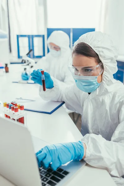 Biotechnologist holding test tube with blood sample and using laptop — Stock Photo