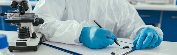 Partial view of biochemist writing results on clipboard in laboratory, panoramic shot — Stock Photo