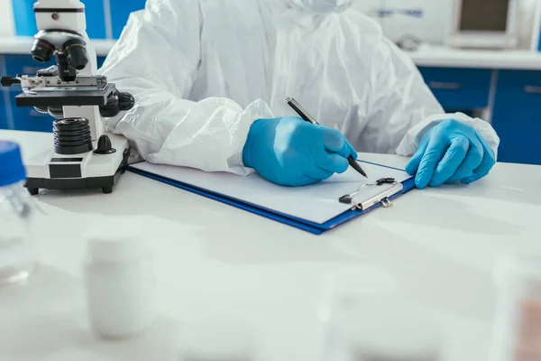 Cropped view of biochemist writing results on clipboard in laboratory — Stock Photo