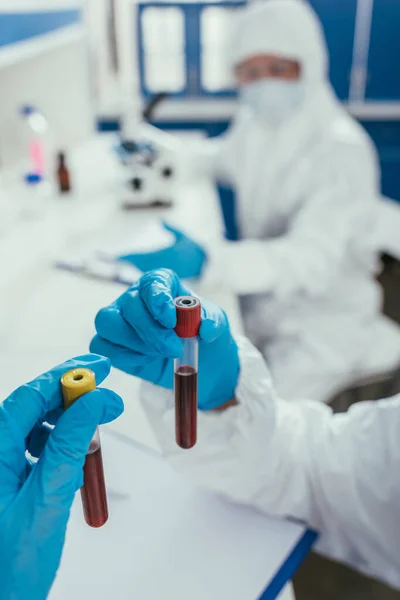 Обрезанный вид биохимика, держащего пробирки с образцами крови рядом с коллегой — стоковое фото
