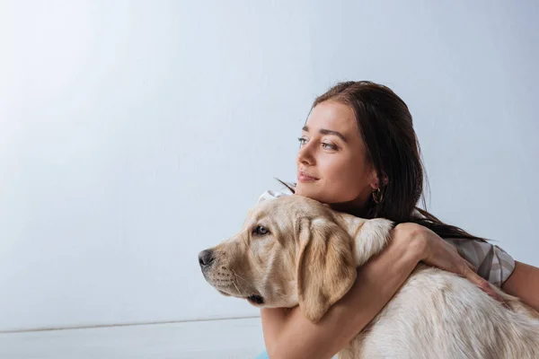 Muchacha atractiva mirando hacia otro lado mientras abraza golden retriever sobre fondo blanco - foto de stock