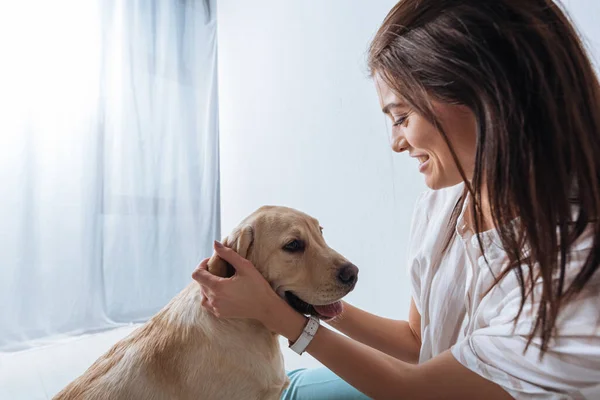 Side view of smiling girl petting golden retriever at home — Stock Photo