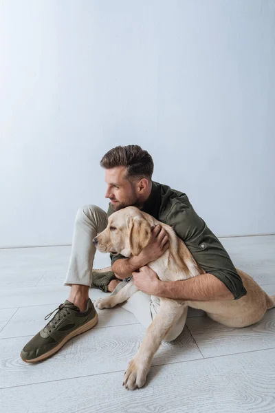 Bello uomo sorridente che abbraccia golden retriever sul pavimento su sfondo bianco — Foto stock