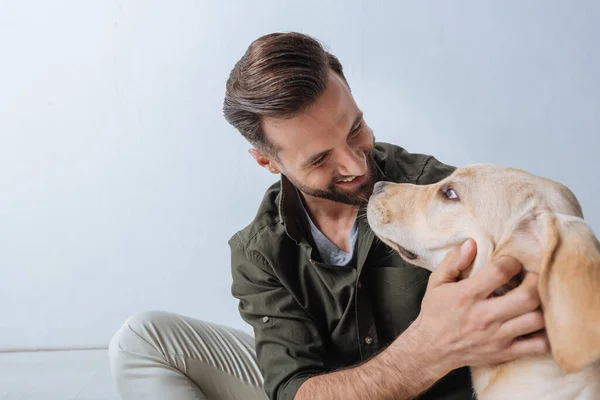 Schöner Mann lächelt Golden Retriever auf weißem Hintergrund an — Stockfoto