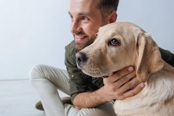 Foco seletivo de golden retriever sentado perto de homem sorridente no fundo branco — Fotografia de Stock