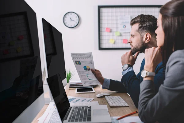 Vista laterale di analisti di sistemi informatici che lavorano con grafici vicino a monitor di computer con schermo vuoto sul tavolo in ufficio — Foto stock