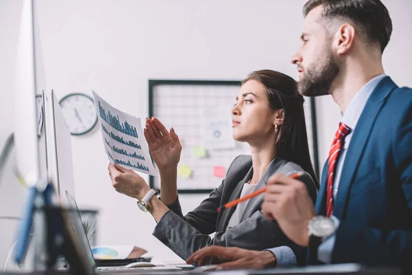 Vista lateral de los analistas de datos utilizando gráficos al evaluar el riesgo en la oficina - foto de stock