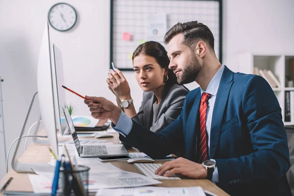 Seitenansicht eines Analytikers für Informationssicherheit, der auf den Computermonitor seines Kollegen zeigt — Stockfoto