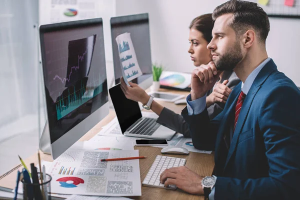 Visão lateral dos analistas que planejam a proteção para sistemas de computador com gráficos em monitores de computador na mesa — Fotografia de Stock