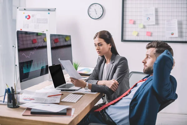 Vista lateral de los analistas de datos que planifican la protección de los sistemas informáticos cerca de gráficos en monitores informáticos - foto de stock