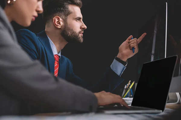 Enfoque selectivo de los analistas de seguridad de la información que trabajan con computadoras portátiles y computadoras en mesa aisladas en negro - foto de stock