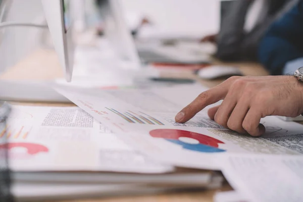 Cropped view of data analyst pointing with finger at charts near computer on table — Stock Photo