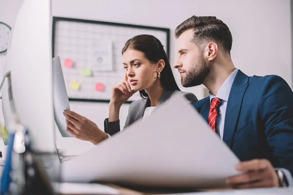 Selektiver Fokus von Computersystemanalysten, die Papiere in der Nähe von Computern auf dem Tisch betrachten — Stockfoto