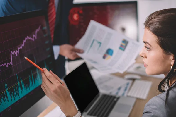 Selective focus of information security analyst pointing on charts on computer monitor near colleague with papers isolated on grey — Stock Photo
