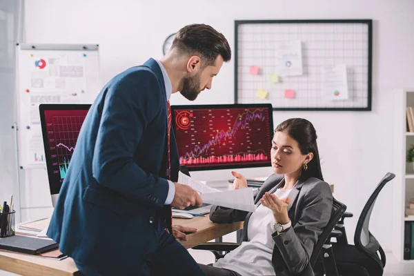 Data analyst holding papers near colleague at table with computers — Stock Photo