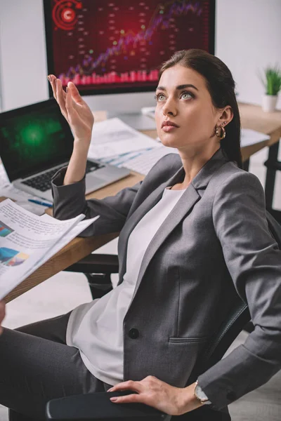 Hermoso analista de sistemas informáticos mirando hacia otro lado cerca de computadoras y papeles en la mesa - foto de stock