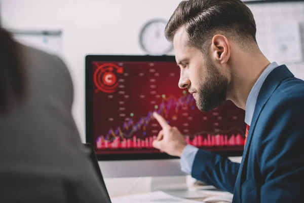 Selective focus of analyst pointing on charts on computer monitor while working with colleague in office — Stock Photo