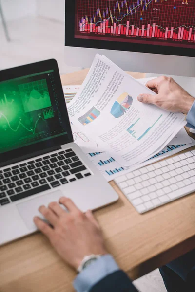 Cropped view of data analyst using laptop and papers with graphs while testing security of computer systems — Stock Photo