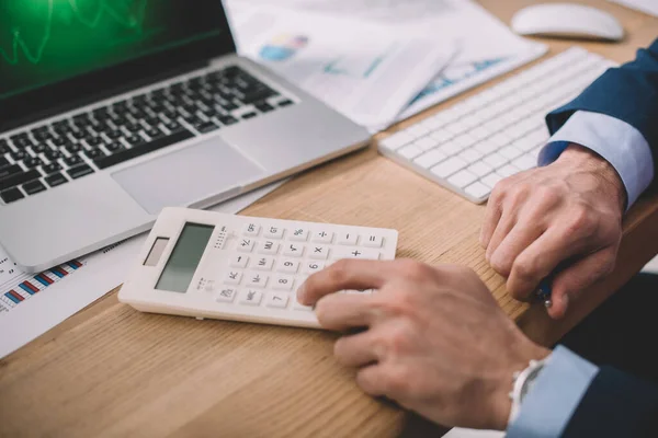 Ausgeschnittene Ansicht des Datenanalysten mit Taschenrechner in der Nähe von Laptop und Papieren auf dem Tisch — Stockfoto