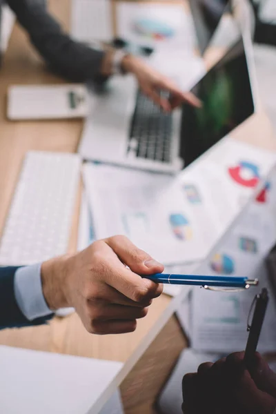 Selective focus of computer systems analyst pointing on computer monitor near colleague with laptop at table — Stock Photo