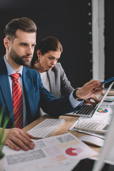 Selektiver Fokus des Datenanalysten beim Arbeiten mit Diagrammen in der Nähe des Kollegen mit Laptop am Tisch — Stockfoto