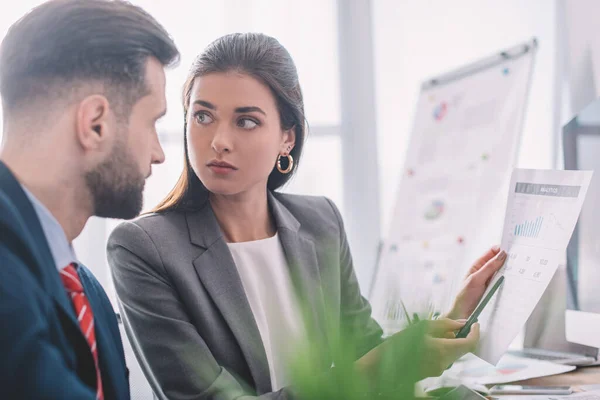 Selective focus of data analyst pointing on chart to colleague in office — Stock Photo