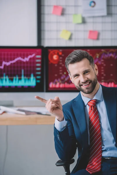 Lächelnder Analyst für Informationssicherheit zeigt mit dem Finger in der Nähe von Computern auf dem Tisch im Büro — Stockfoto