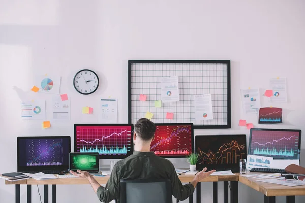 Vista posterior de los analistas de datos sentados en la mesa con computadoras y gráficos en la oficina - foto de stock