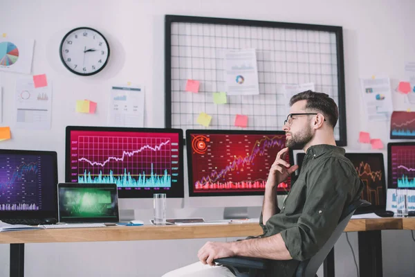 Vista laterale dell'analista di dati pensieroso che guarda lontano vicino ai grafici sui monitor del computer in ufficio — Foto stock