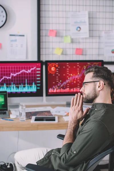 Side view of serious data analyst sitting at table with computers in office — Stock Photo