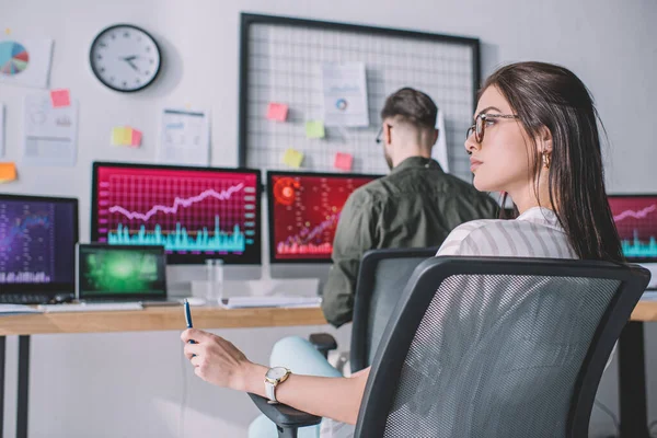 Selective focus of data analyst holding pen near colleague working with computers at table — Stock Photo