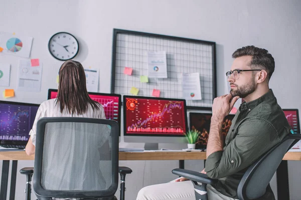 Pensive data analyst looking away near colleague working with computers in office — Stock Photo