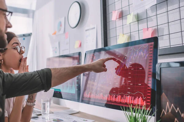 Selective focus of data analyst pointing on charts on computer monitor at shocked colleague — Stock Photo