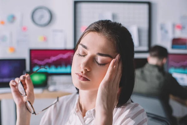 Selective focus of tired data analyst touching head while colleague working in office — Stock Photo