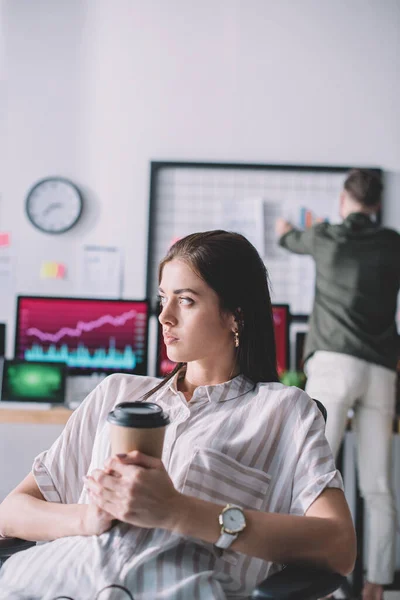 Selective focus of computer systems analyst holding paper cup while colleague in office — Stock Photo