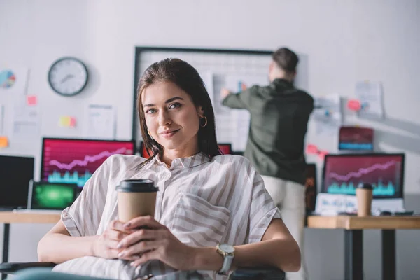 Smiling data analyst holding coffee to go while colleague working in office — Stock Photo