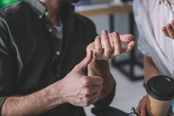 Cropped view of data analyst showing thumb up gesture to colleague with coffee to go — Stock Photo