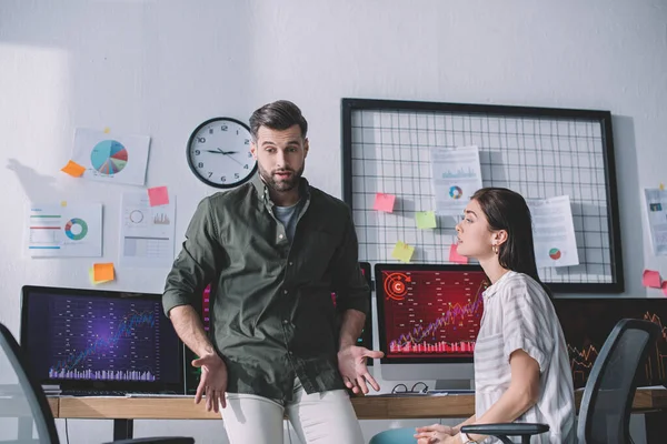 Data analyst looking at confused colleague near computers on table in office — Stock Photo