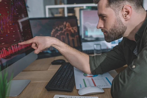 Side view of information security analyst pointing with finger on charts on computer monitor while working in office — Stock Photo