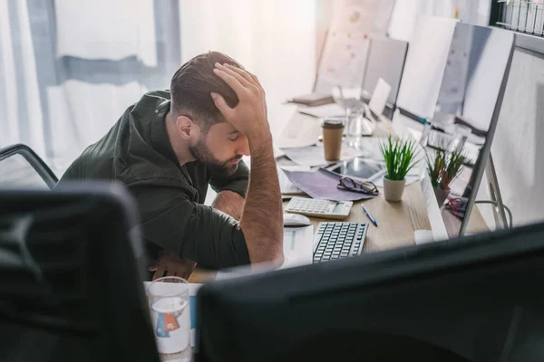 Enfoque selectivo del analista de datos con la mano cerca de la cabeza sentada a la mesa con dispositivos digitales - foto de stock