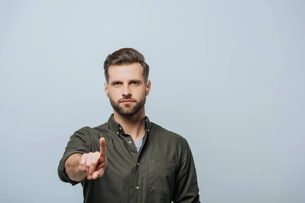 Schöner Mann, der mit dem Finger zeigt und isoliert auf graue Kamera schaut — Stockfoto