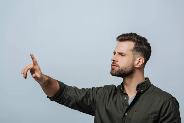 Schöner Mann, der etwas Isoliertes auf Grau berührt — Stockfoto