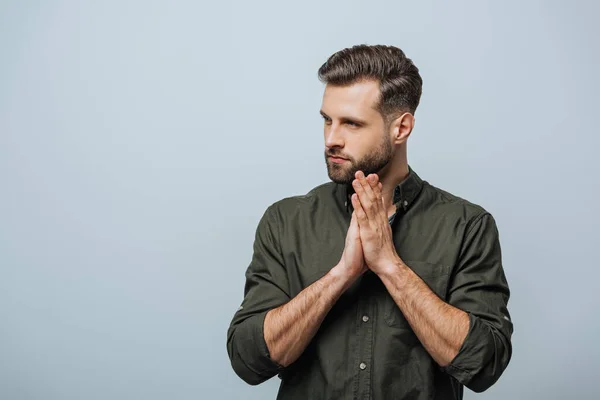 Bello uomo barbuto con le mani in preghiera distogliendo lo sguardo isolato sul grigio — Foto stock