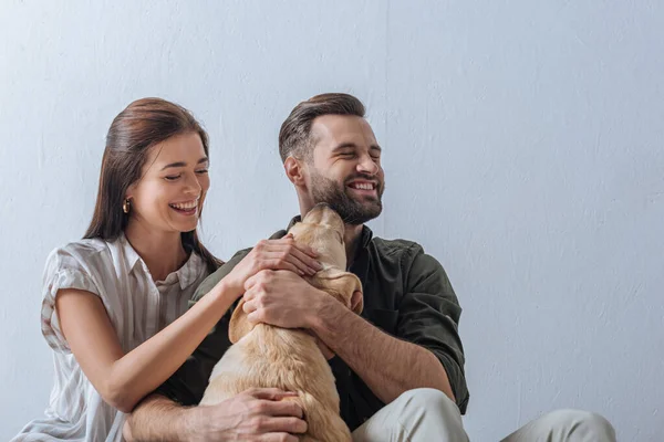 Fröhliches junges Paar umarmt Golden Retriever auf grauem Hintergrund — Stockfoto