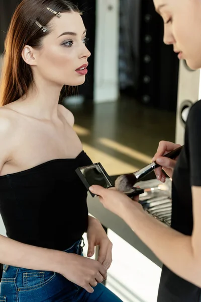 Messa a fuoco selettiva di trucco artista tenendo pennello cosmetico e cipria vicino al modello — Foto stock