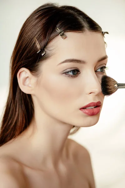 Cepillo cosmético con polvo facial cerca de mujer atractiva en blanco - foto de stock