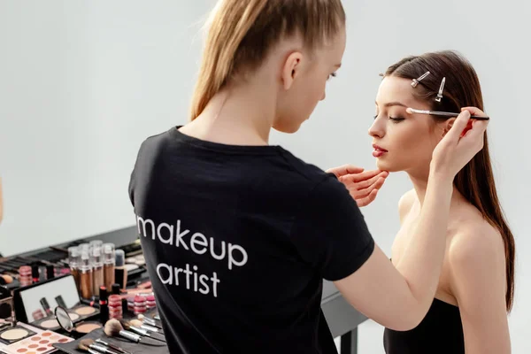 Woman in black t-shirt with makeup artist lettering applying eye shadow on model — Stock Photo