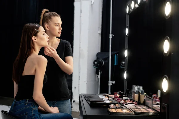 Artista de maquiagem tocando rosto de modelo atraente e olhando para o espelho — Fotografia de Stock