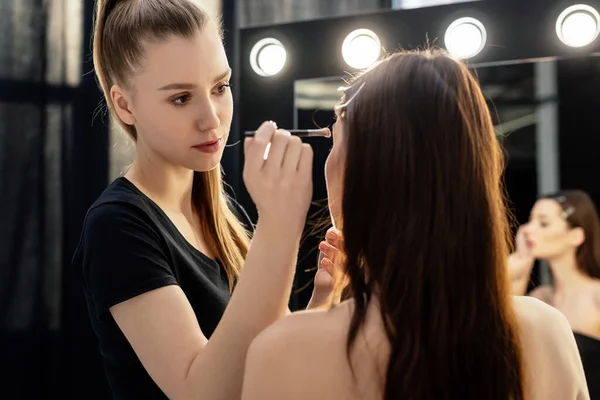 Artista de maquiagem segurando escova cosmética perto do modelo no estúdio de fotos — Fotografia de Stock