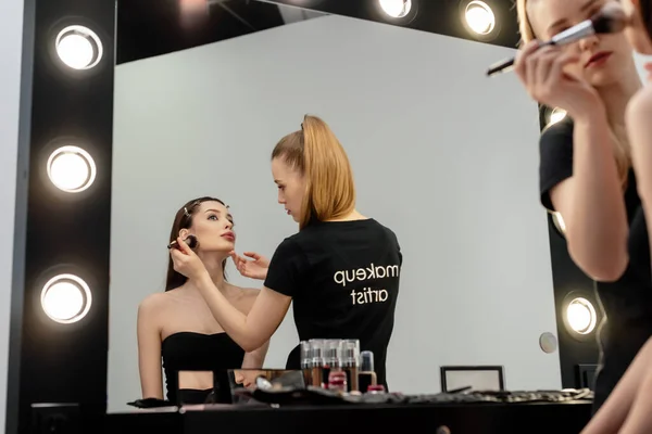 Mulher em t-shirt preta com maquiagem artista lettering aplicando pó facial no modelo — Fotografia de Stock